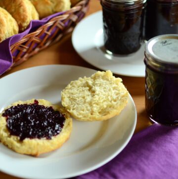 blackberry jam on biscuit with blackberry jam jar and biscuits in a basket with purple napkin